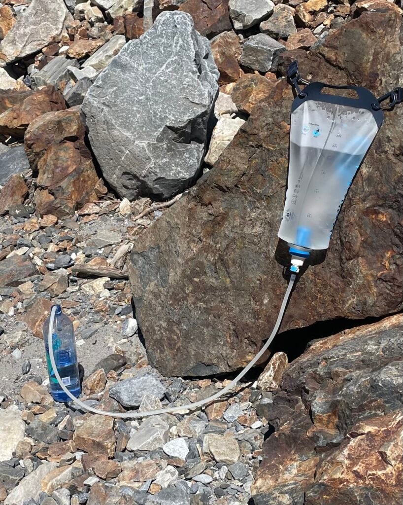 My ketadyne gravity water filter on top of a rock filtering water into a plastic bottle.