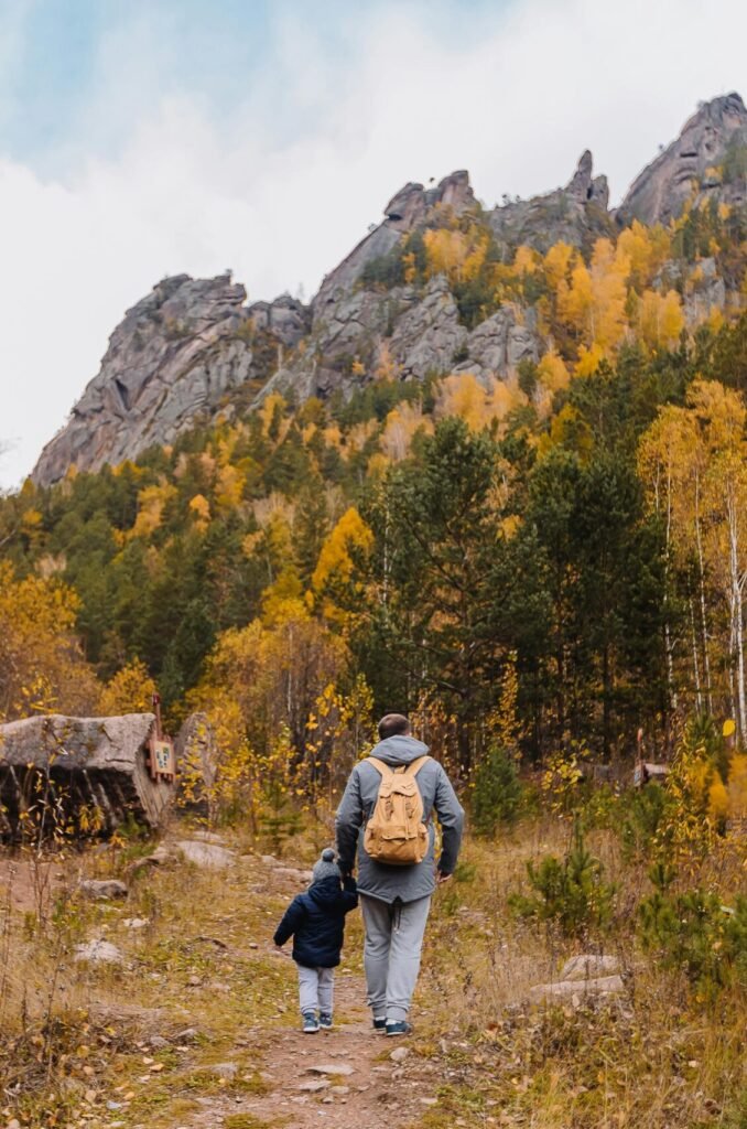 A father and son hiking together in an autumn mountain forest, surrounded by colorful trees.