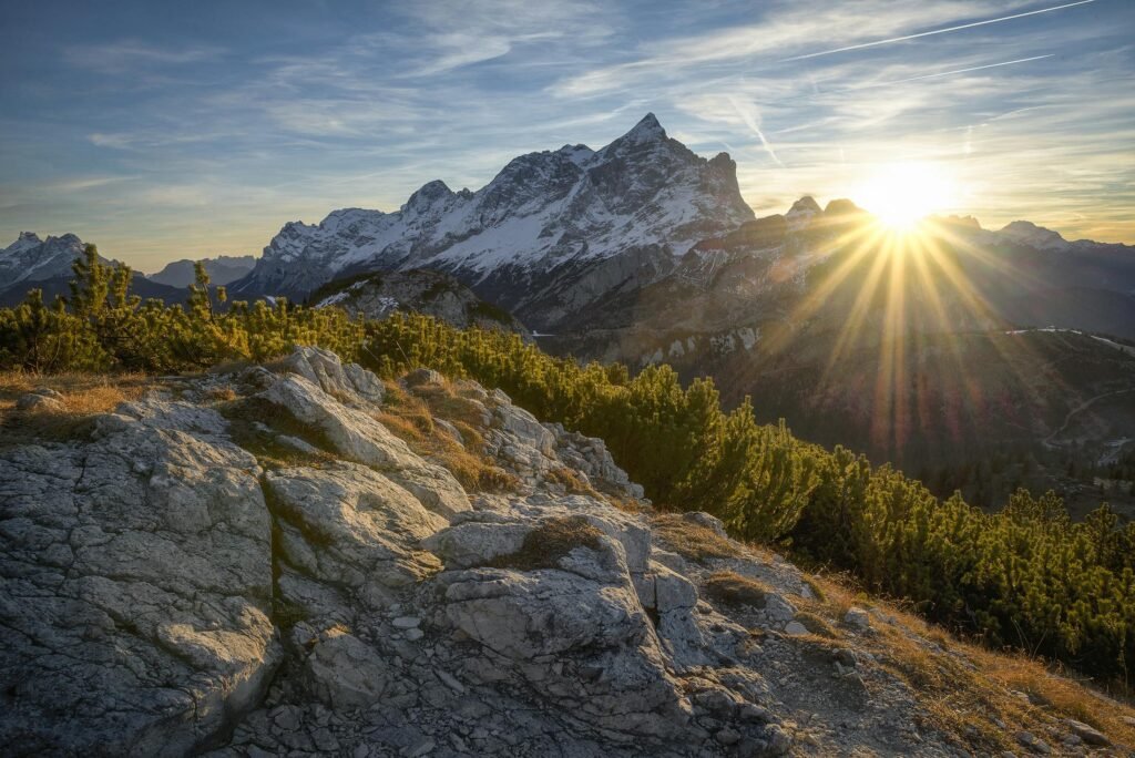 Stunning sunrise casting rays over the Italian Alps in Alleghe, Veneto, with lush greenery and rocky terrain showcasing the best quotes about wilderness.