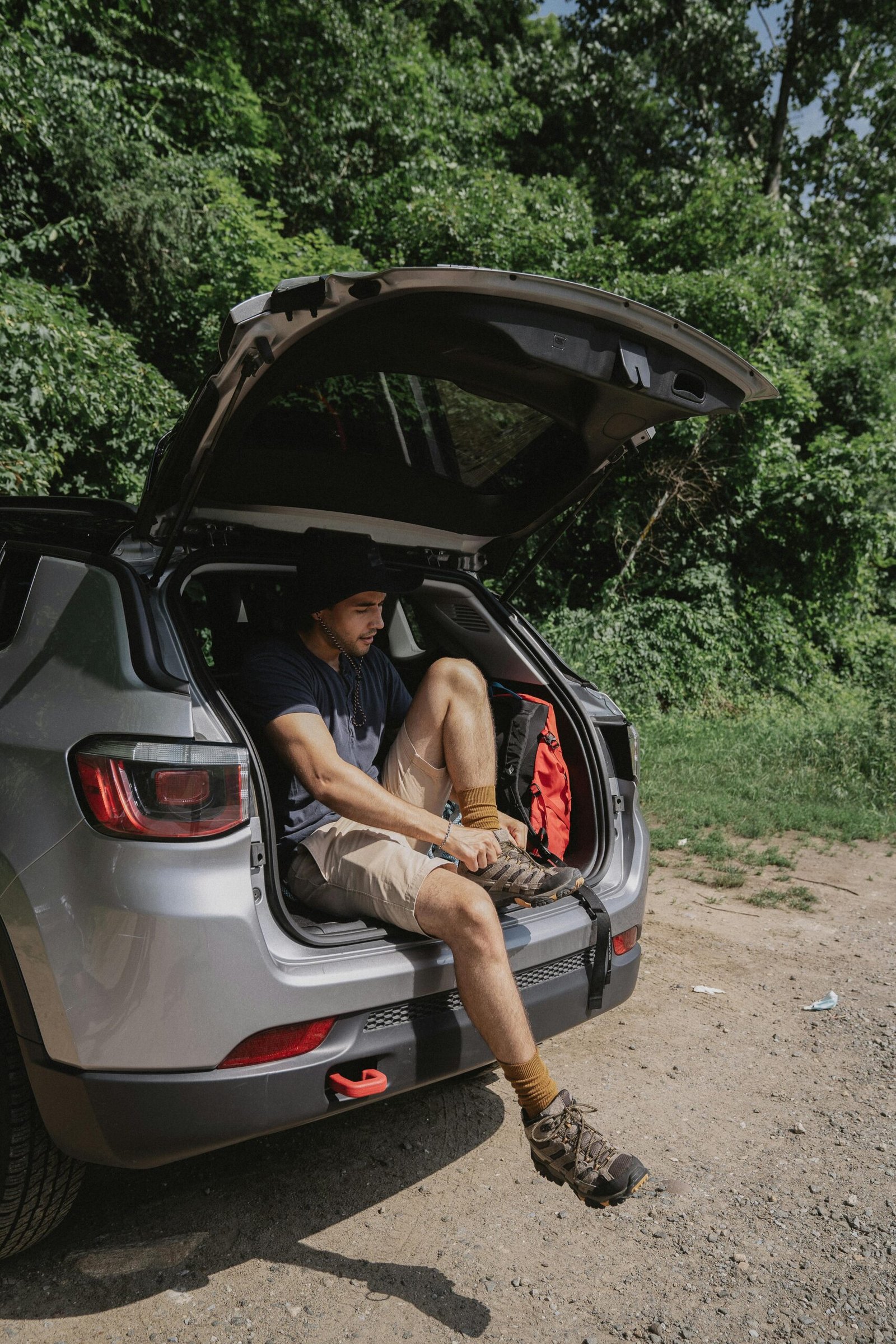 Adult man sitting at car trunk, putting on danner hiking boots before an outdoor trek.