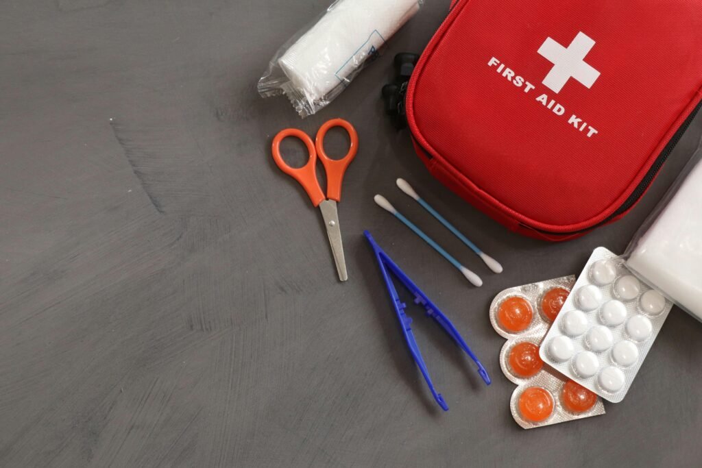 A red first aid kit with medicine, scissors, tweezers and gauze.