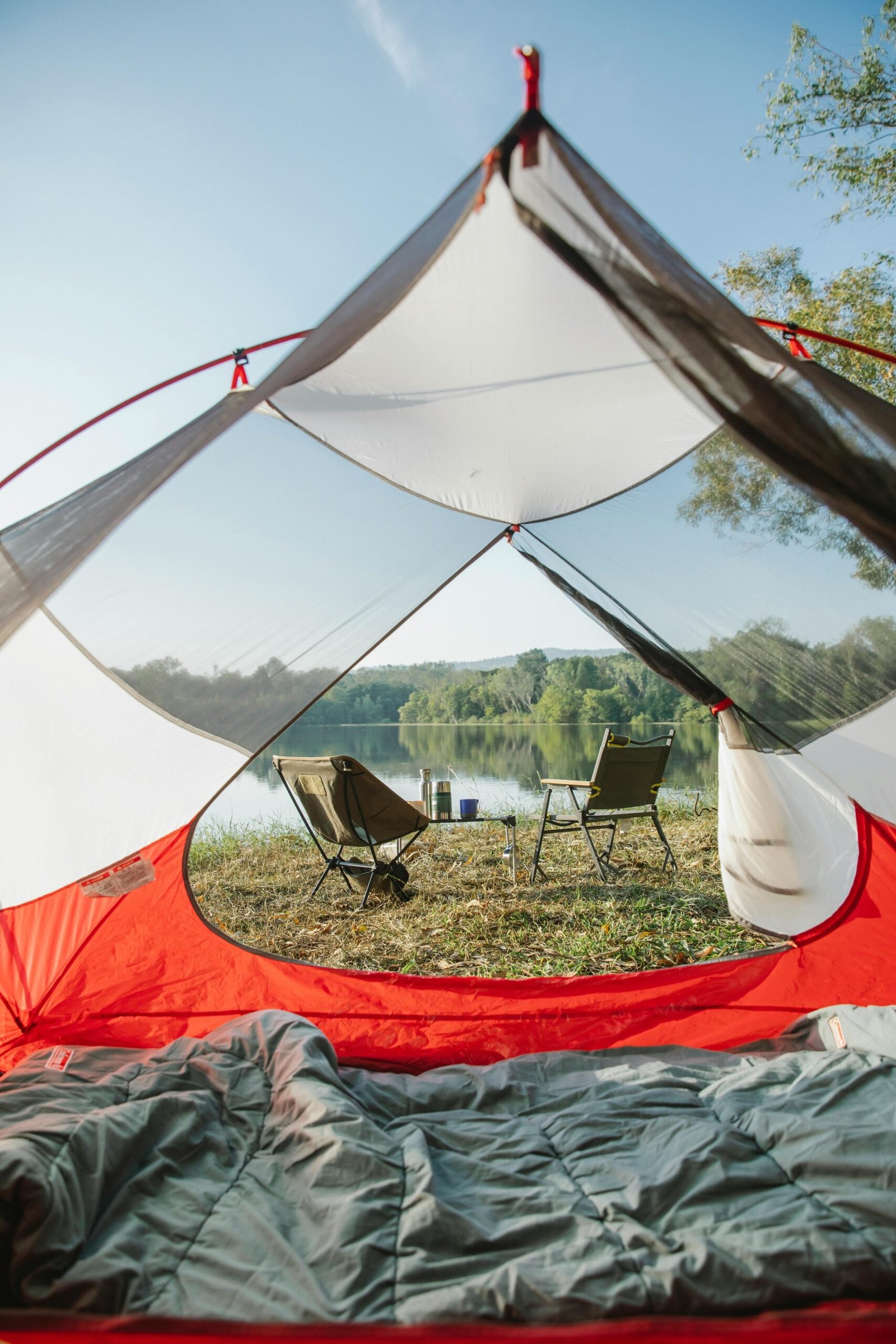 View thought empty camping tent on grassy coast with chairs placed near calm river in countryside in sunny day