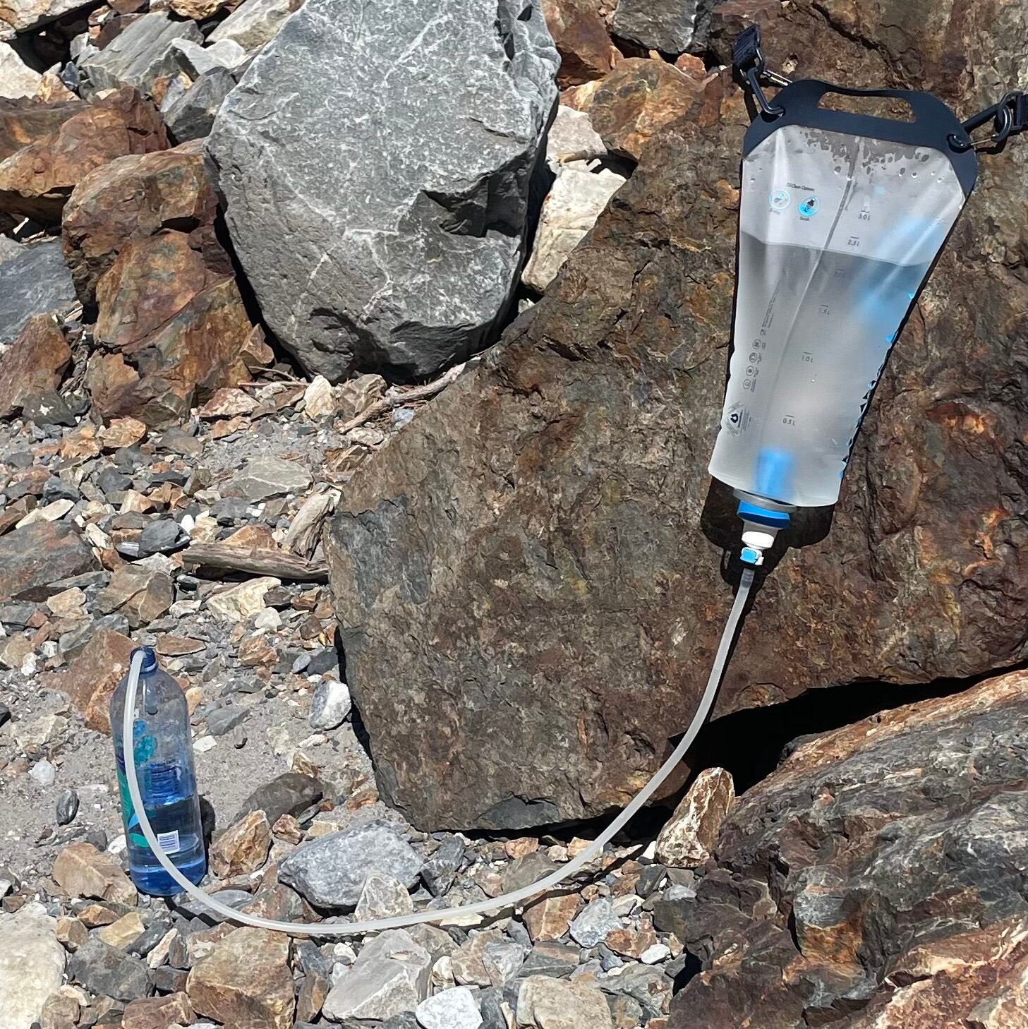 My ketadyne gravity water filter on top of a rock filtering water into a plastic bottle. Best survival water filters 2026.